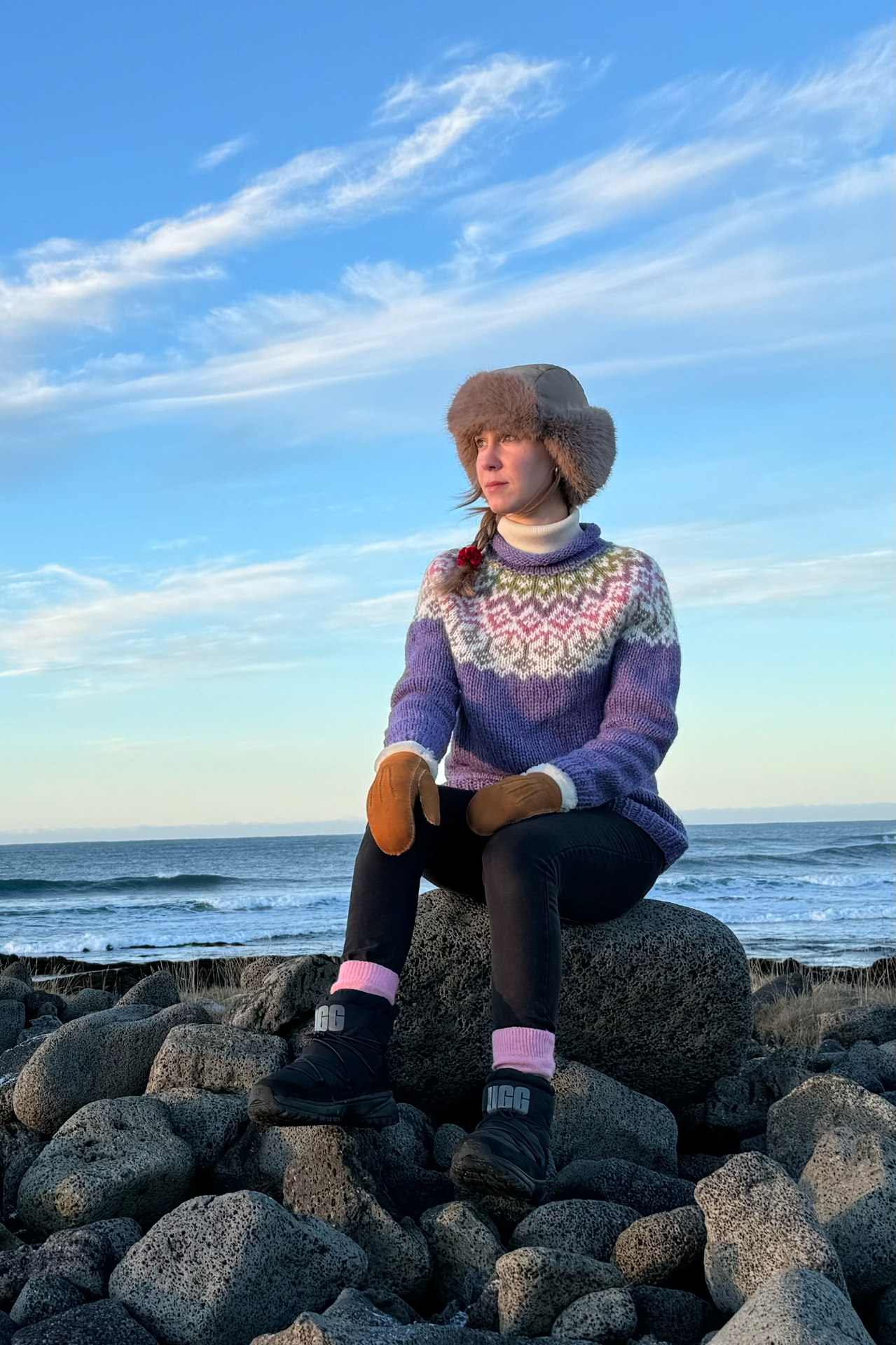 Person sitzt auf Felsen am Meer, trägt